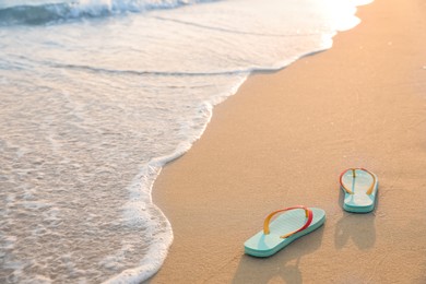 Bright turquoise beach slippers on sand near sea, space for text