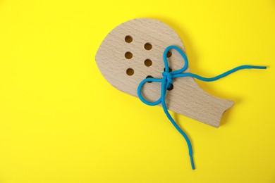 Photo of Wooden figure with holes and lace on yellow background, top view and space for text. Educational toy for motor skills development