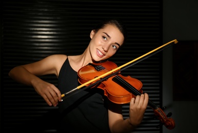 Photo of Beautiful young woman playing violin in dark room