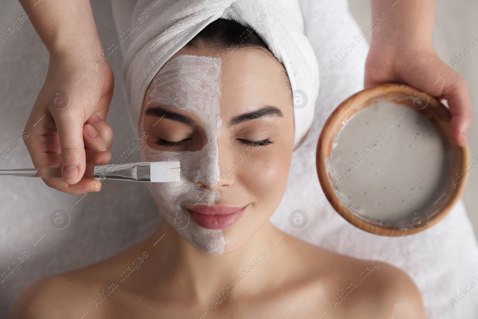 Photo of Cosmetologist applying mask on woman's face in spa salon, closeup. Top view