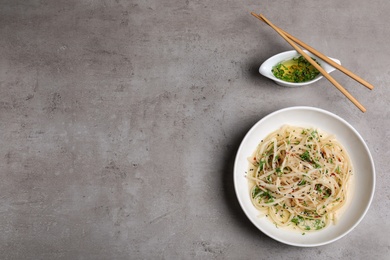 Plate of noodles with broth served on grey background, flat lay. Space for text