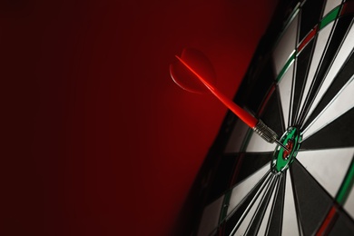 Photo of Color arrow hitting target on dart board against red background. Space for text