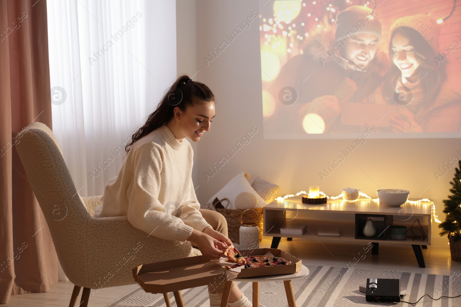 Photo of Woman with pizza watching romantic Christmas movie via video projector at home