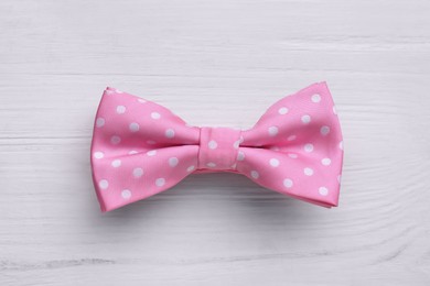 Stylish pink bow tie with polka dot pattern on white wooden table, top view