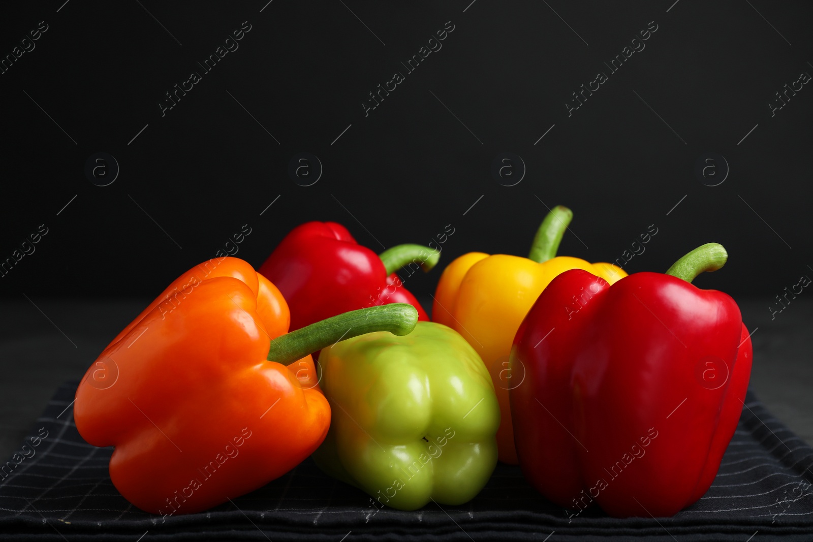 Photo of Fresh ripe bell peppers on tablecloth against black background