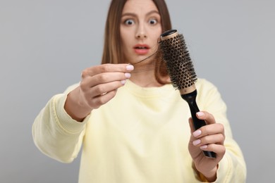 Photo of Woman untangling her lost hair from brush on light grey background, selective focus. Alopecia problem