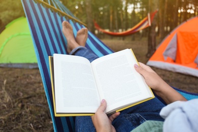 Woman with book resting in comfortable hammock outdoors, closeup