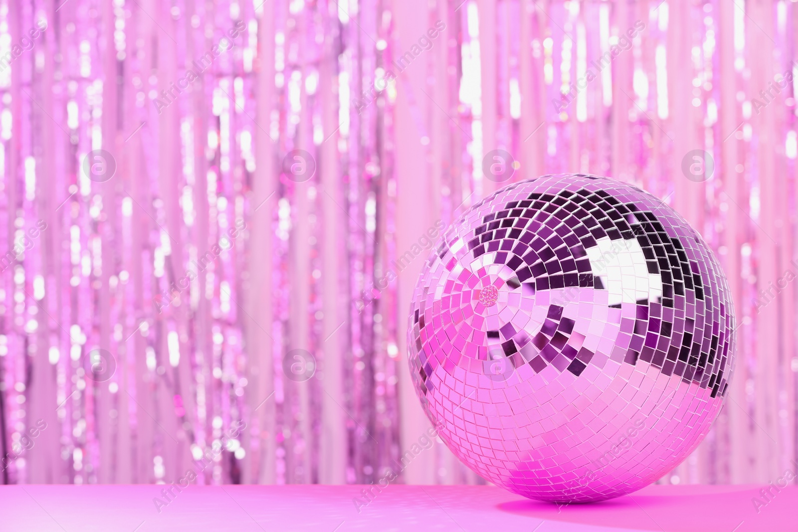 Photo of Shiny disco ball on table against blurred background, toned in pink. Space for text