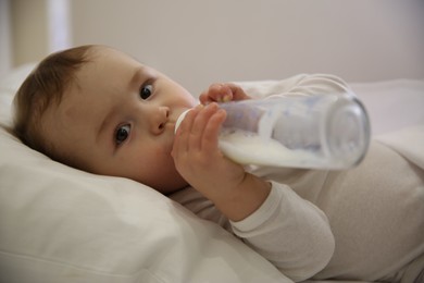 Photo of Cute little baby with bottle lying in comfortable crib. Bedtime