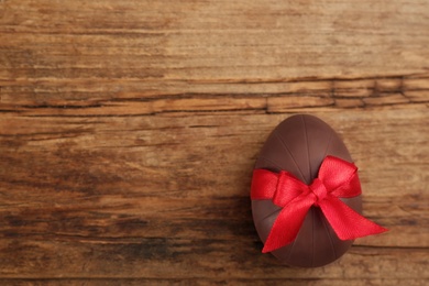 Photo of Sweet chocolate egg with red bow on wooden table, top view. Space for text