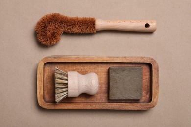 Photo of Cleaning brushes and soap bar on pale brown background, top view