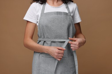 Photo of Woman wearing kitchen apron on brown background, closeup. Mockup for design