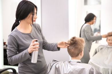 Photo of Professional female hairdresser working with little boy in salon