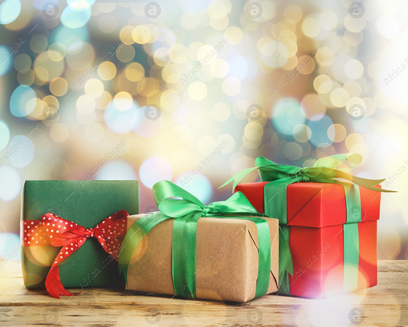 Image of Christmas gift boxes on wooden table against blurred background, bokeh effect