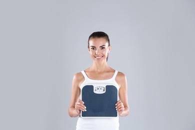 Photo of Happy young woman with scales on color background. Weight loss motivation