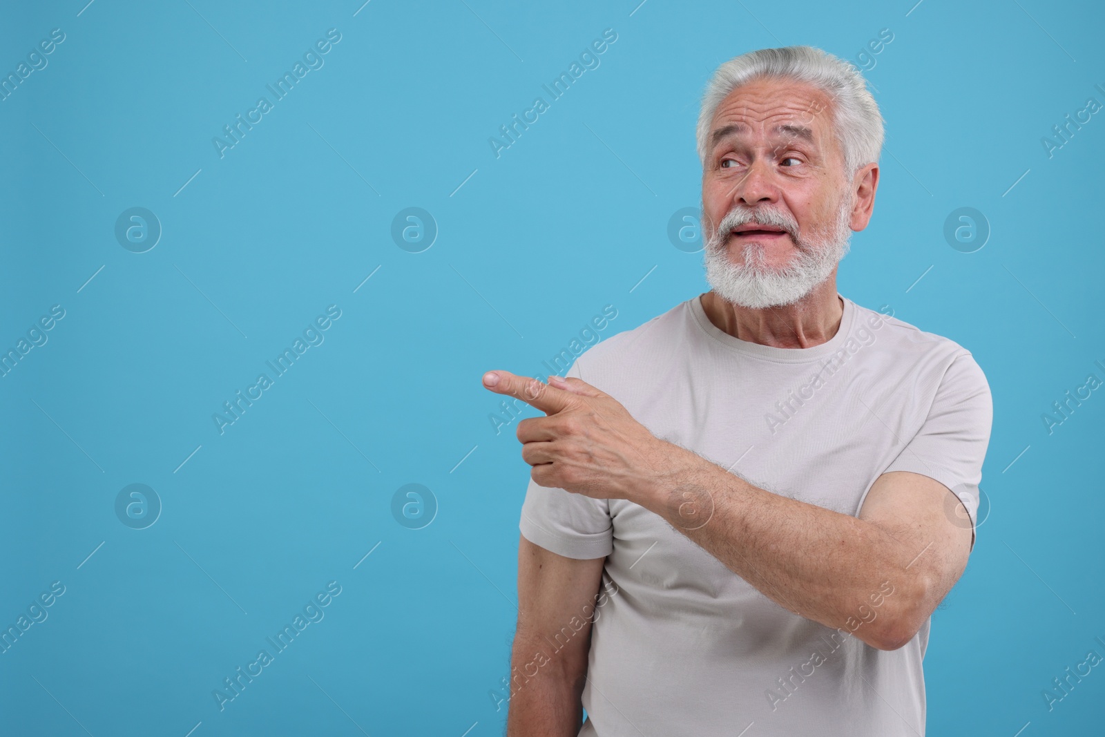 Photo of Special promotion. Senior man pointing at something on light blue background. Space for text