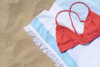 Photo of White and light blue striped towel with bikini top on sandy beach, flat lay. Space for text