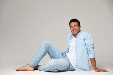 Handsome young African-American man sitting on light background