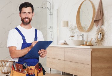 Plumber with clipboard and tool belt in bathroom, space for text