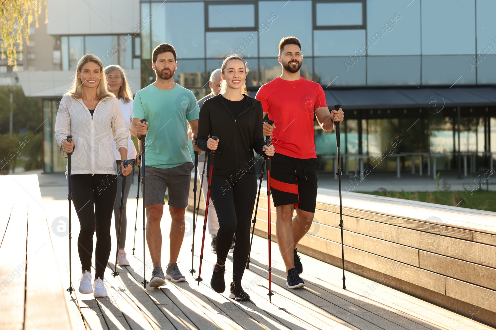 Photo of Group of people practicing Nordic walking with poles outdoors on sunny day