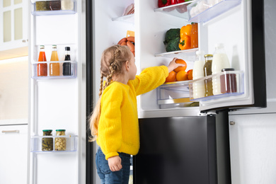 Little girl taking orange out if refrigerator in kitchen