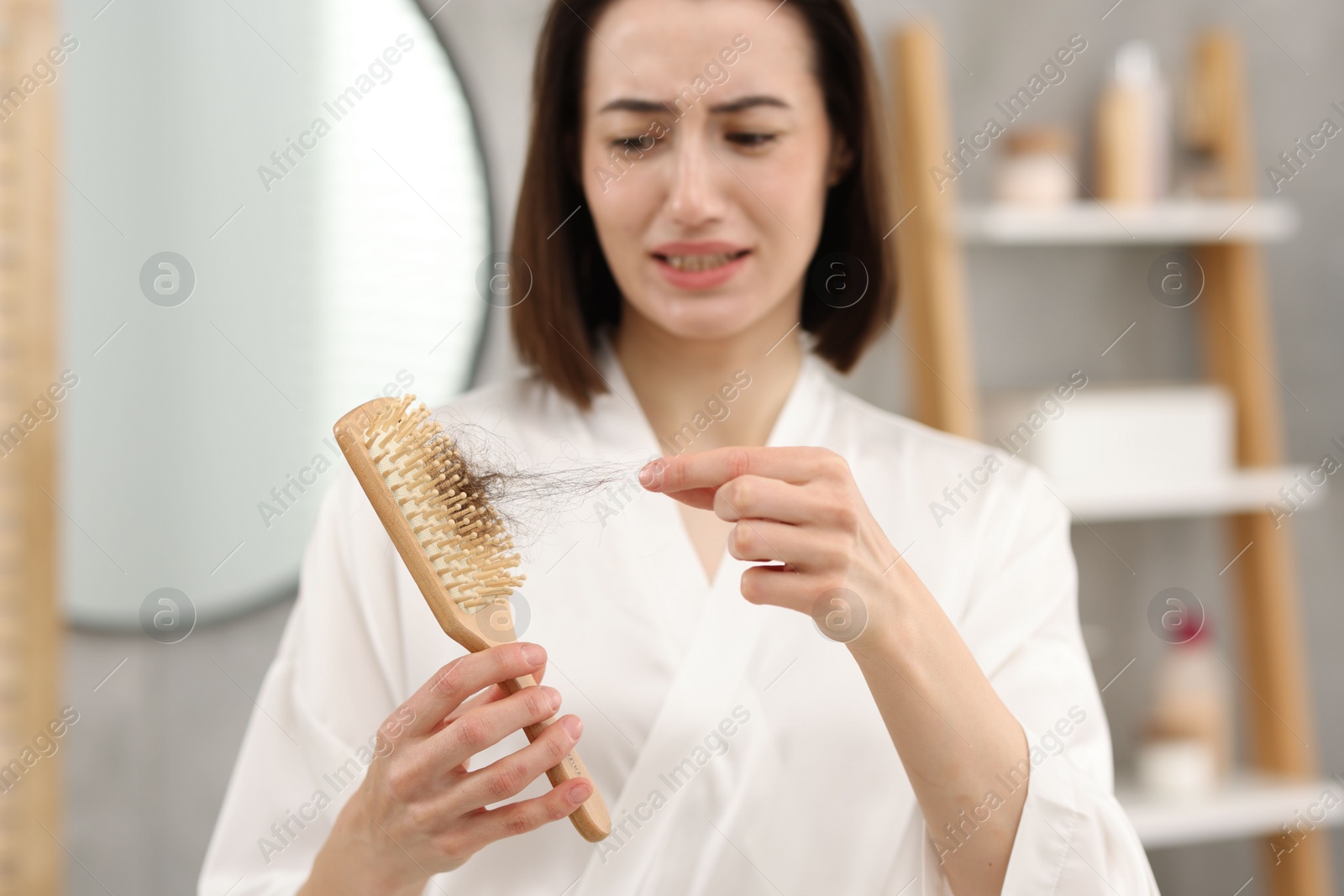Photo of Stressed woman taking her lost hair from brush in bathroom, selective focus. Alopecia problem