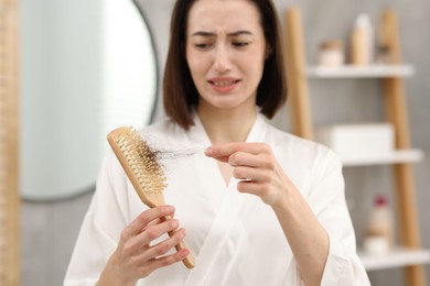 Photo of Stressed woman taking her lost hair from brush in bathroom, selective focus. Alopecia problem