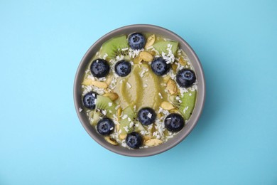 Photo of Bowl of delicious fruit smoothie with fresh blueberries, kiwi slices and coconut flakes on light blue background, top view