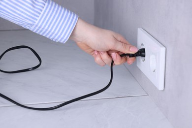 Photo of Woman inserting electric plug into socket at white table indoors, closeup
