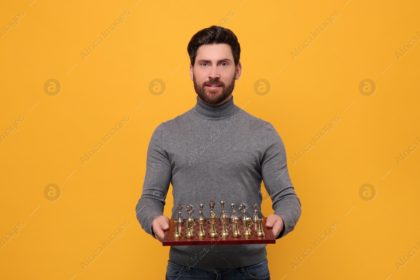 Photo of Handsome man holding chessboard with game pieces on yellow background