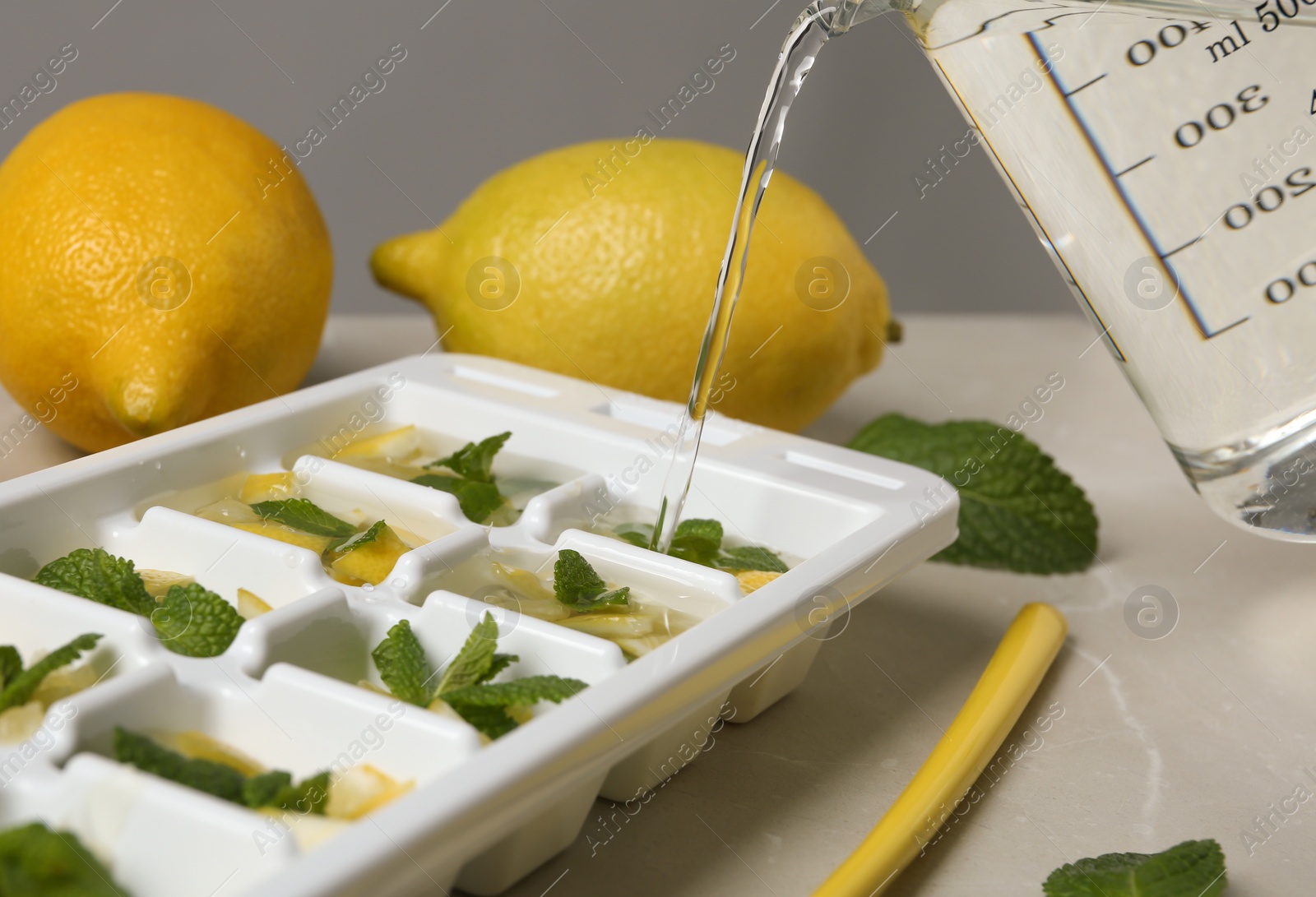 Photo of Pouring water into ice cube tray with mint and lemon on table