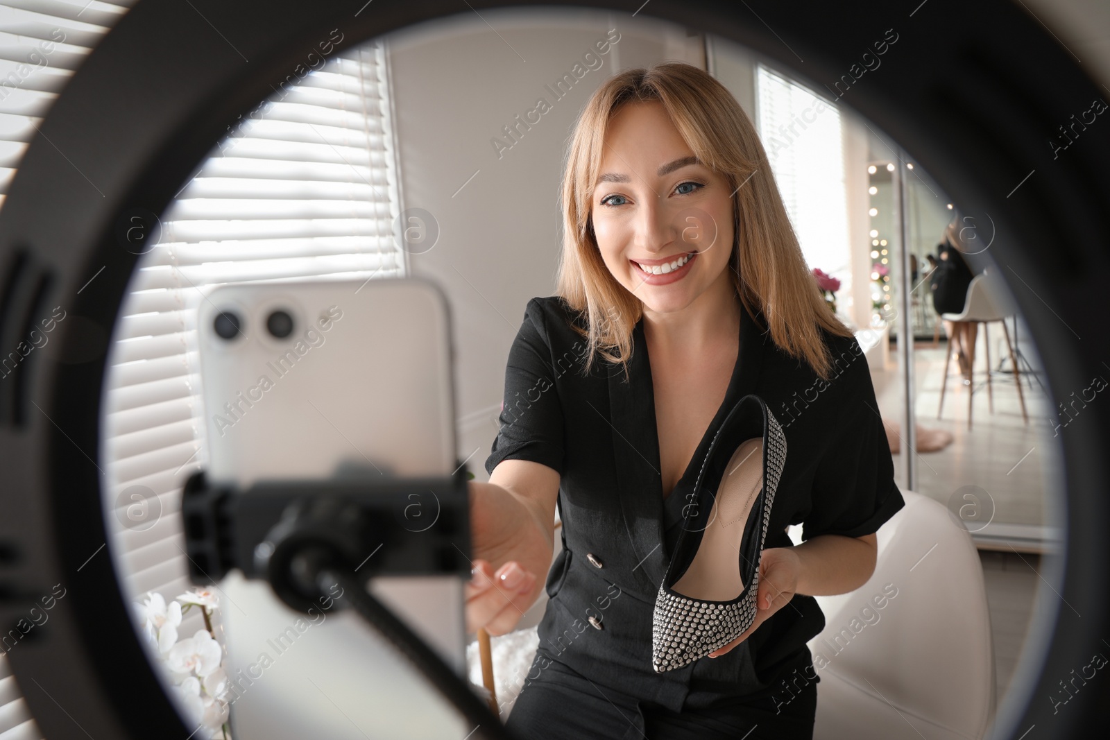 Photo of Fashion blogger with shoe recording video in dressing room at home, view through ring lamp