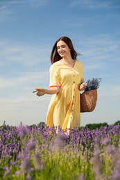 Photo of Young woman with wicker handbag full of lavender flowers in field on summer day