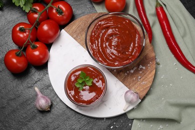 Photo of Organic ketchup in bowls and ingredients on black table, flat lay. Tomato sauce