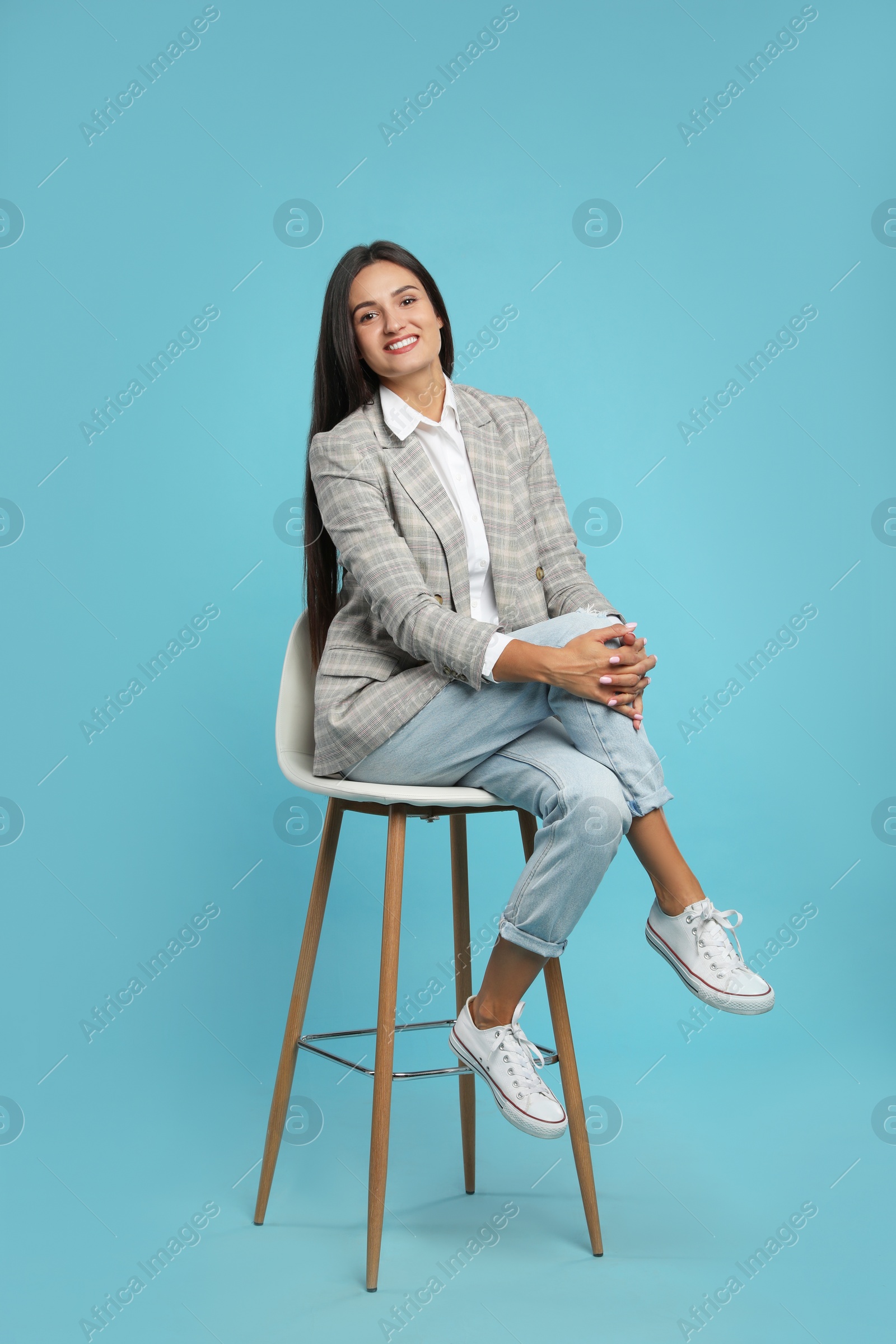 Photo of Beautiful young woman sitting on stool against turquoise background