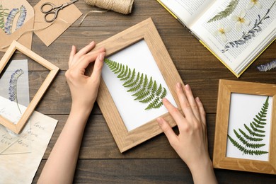 Photo of Woman making beautiful herbarium with pressed dried fern leaf at wooden table, top view.