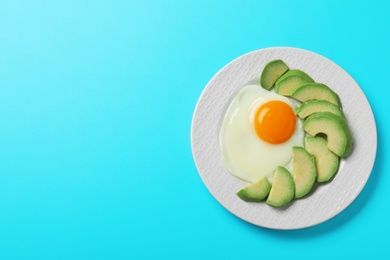 Photo of Plate of fried egg and avocado on light blue background, top view with space for text. Healthy breakfast
