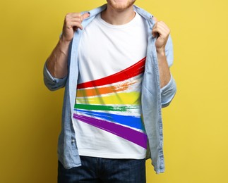 Image of Young man wearing white t-shirt with image of LGBT pride flag on yellow background