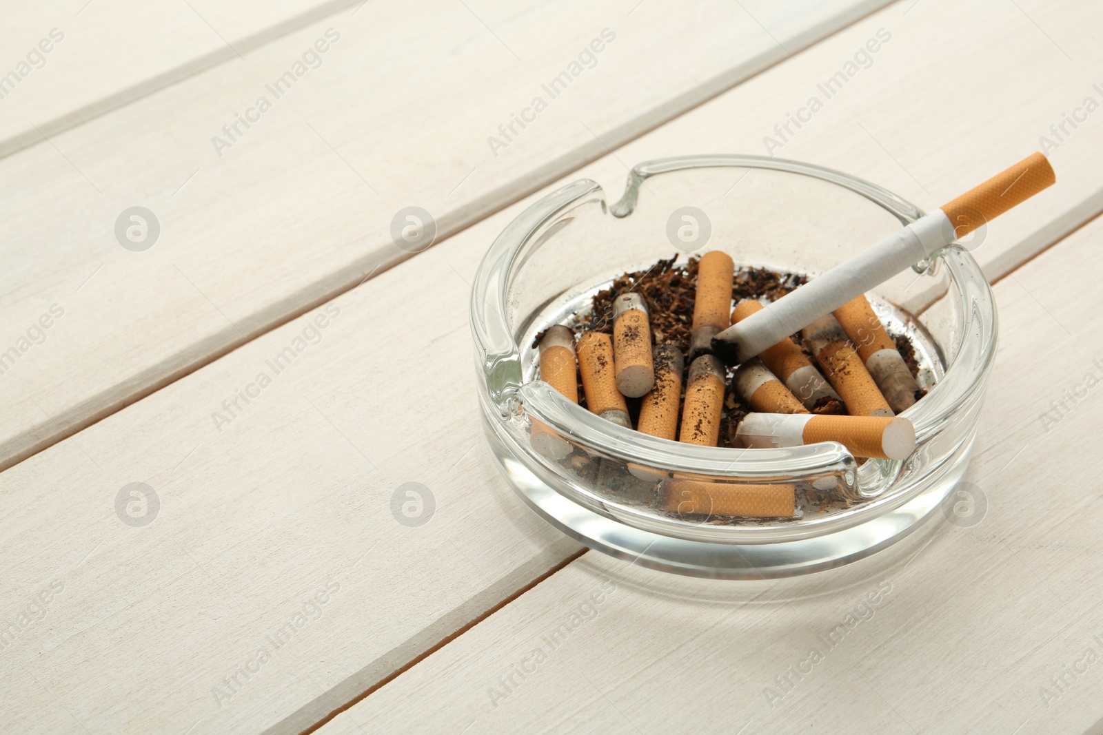 Photo of Glass ashtray with cigarette stubs on white wooden table. Space for text