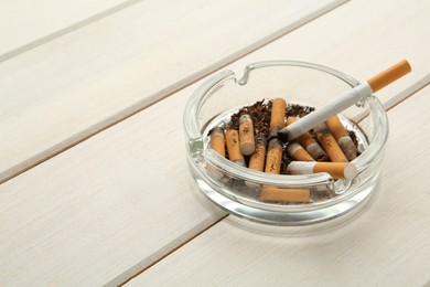 Glass ashtray with cigarette stubs on white wooden table. Space for text
