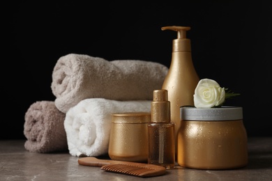 Different hair products, rolled towels and comb on grey table