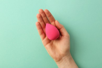 Photo of Woman with pink makeup sponge on mint color background, top view