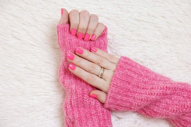 Photo of Woman showing her manicured hands with pink nail polish on faux fur mat, top view