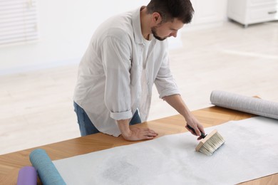 Man applying glue onto wallpaper sheet at wooden table indoors