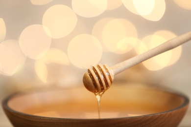 Photo of Honey dripping from dipper into bowl against blurred lights, closeup