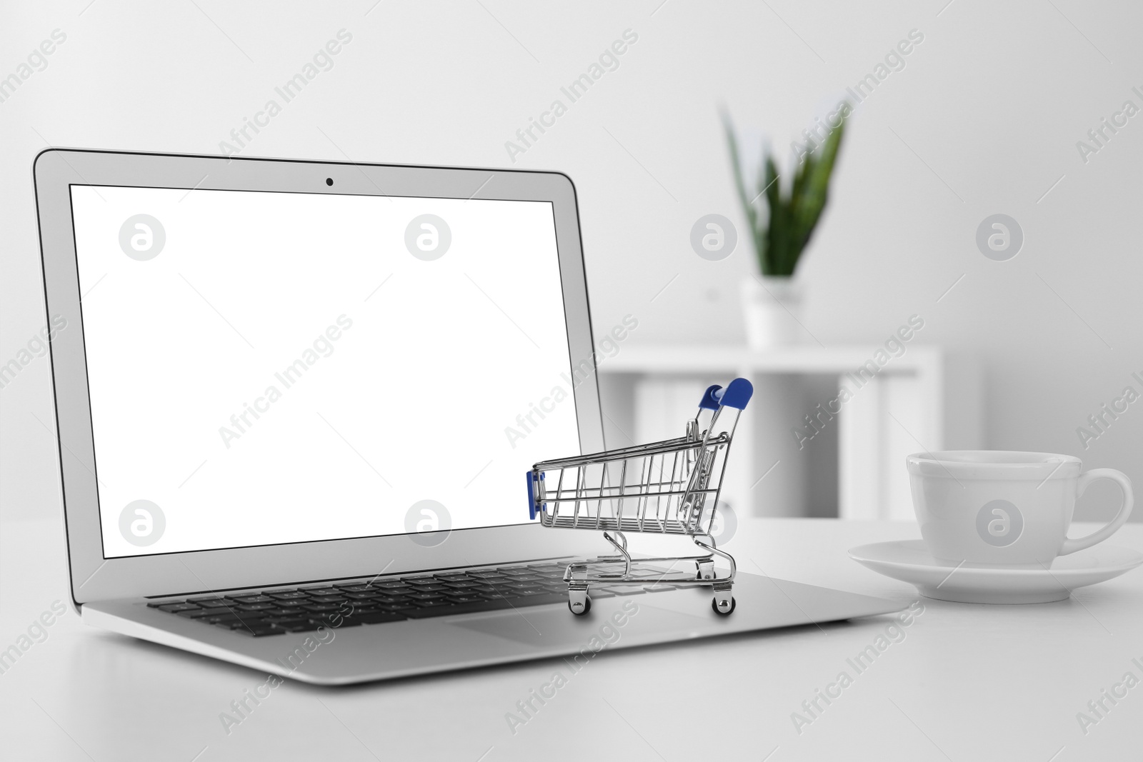 Image of Online shopping. Laptop with small cart and cup on table