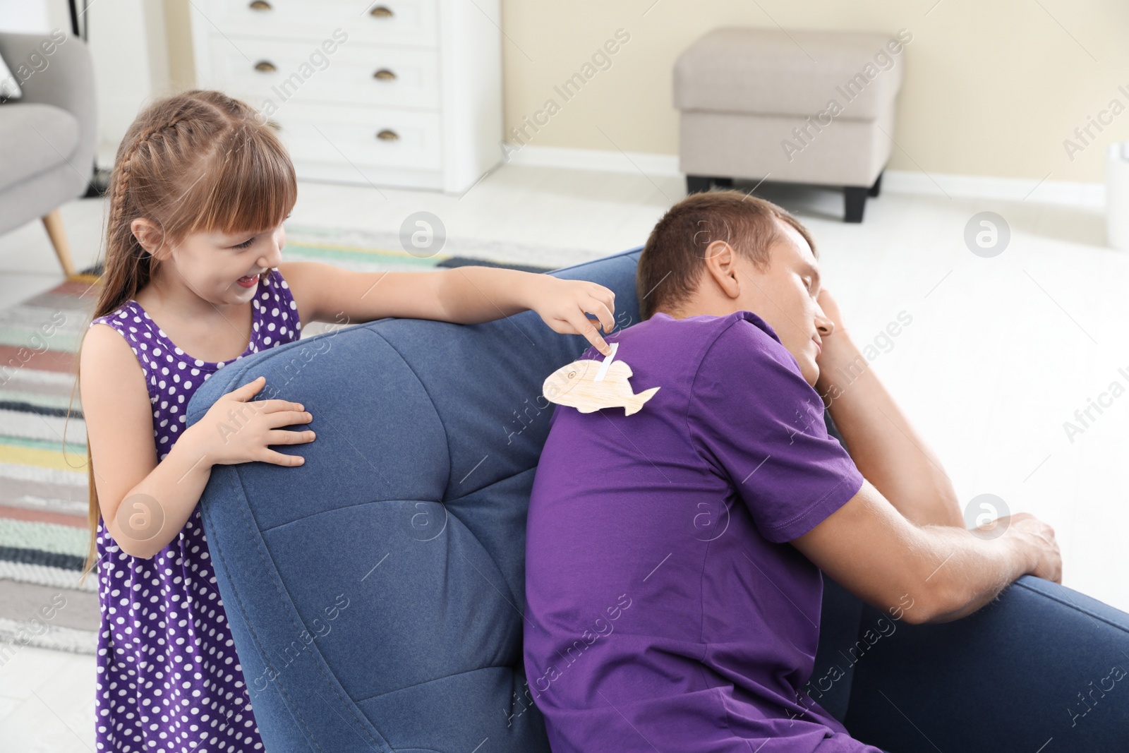 Photo of Child sticking paper fish to father's back on April Fool's Day