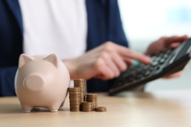 Photo of Financial savings. Man using calculator at wooden table, focus on piggy bank and stacked coins