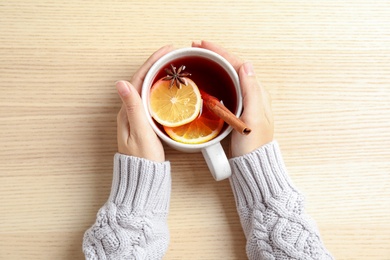 Photo of Woman in warm sweater with cup of hot winter drink on wooden background, top view. Cozy season