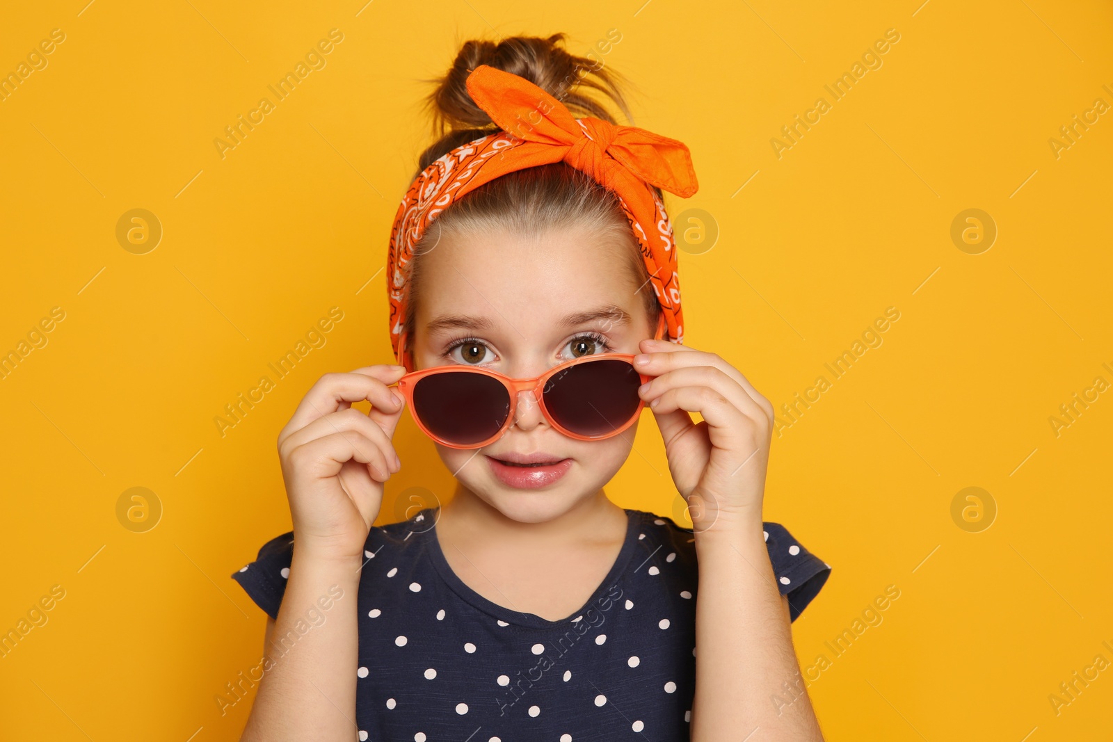 Photo of Cute little girl wearing stylish bandana and sunglasses on orange background